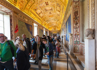 A group of tourists exploring the ornate hallway filled with colorful murals and intricate statues, with an intricately painted ceiling that includes various ancient figures and symbols, within the Sistine Chapel at the Vatican.